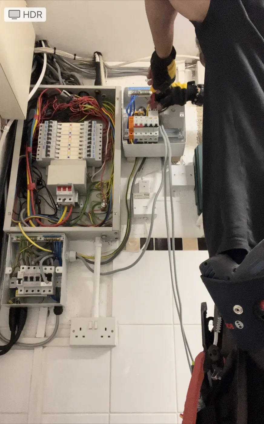 Electrician adding a new consumer unit beside existing three-phase distribution boards
