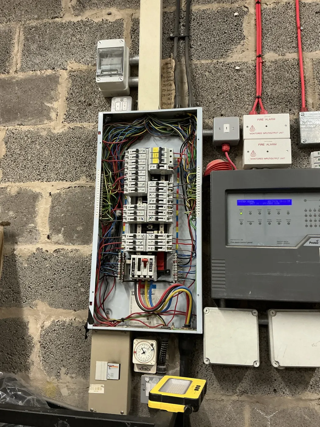 Older commercial distribution board with crowded wiring next to a fire alarm panel