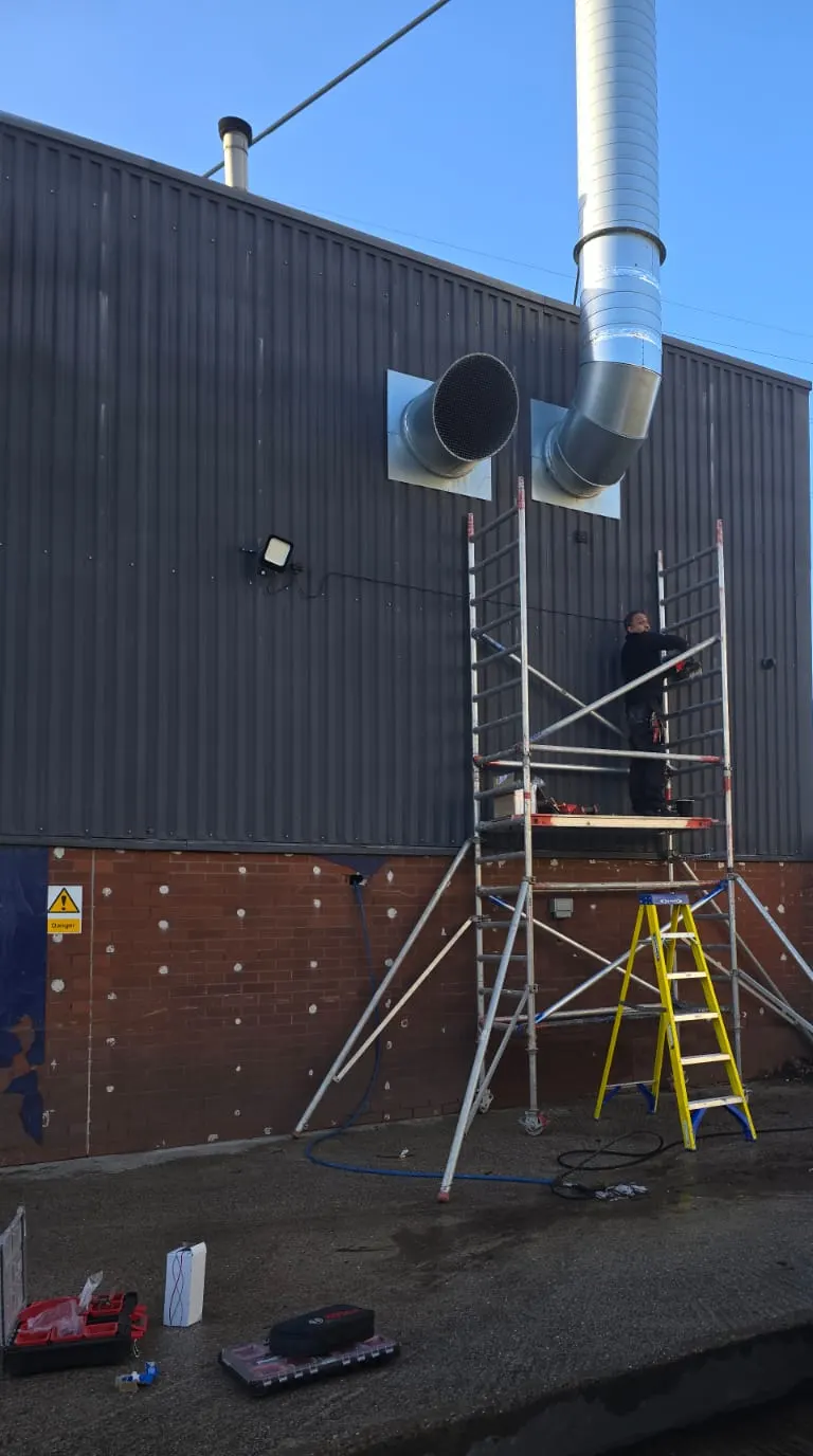 Electrician on a tower scaffold fitting external lighting to an industrial unit