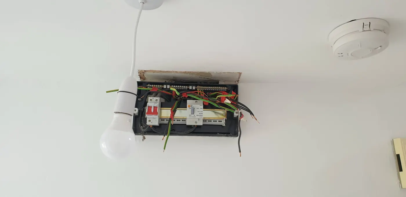 Old consumer unit with cover off and taped, untidy wiring