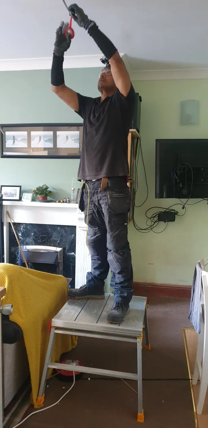 SmartWired electrician in PPE working on a ceiling light connection in a customer’s living room