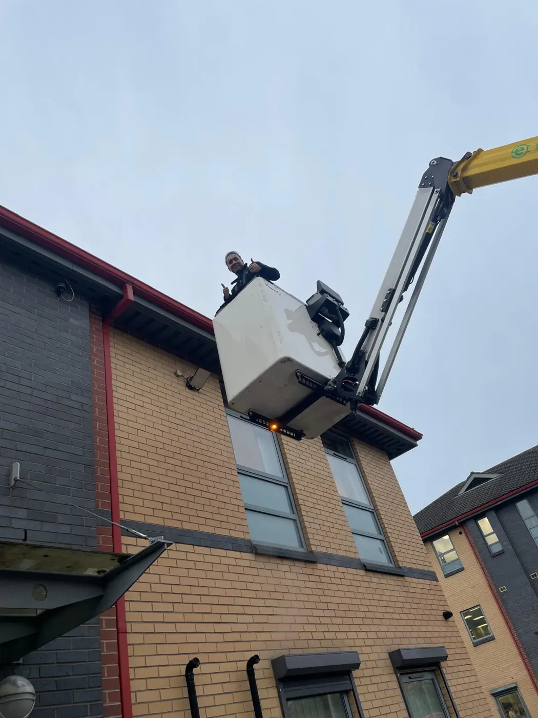 Electrician in a cherry picker working at the eaves of an office building