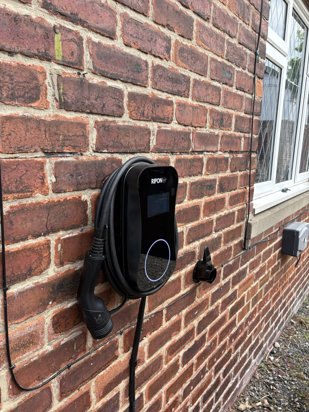 RiponEV display charger on red brick with the supply cable clipped along the wall