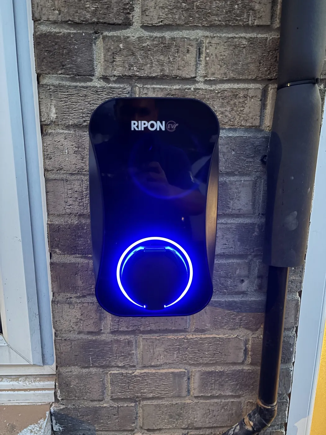 RiponEV charger glowing blue on a dark brick wall