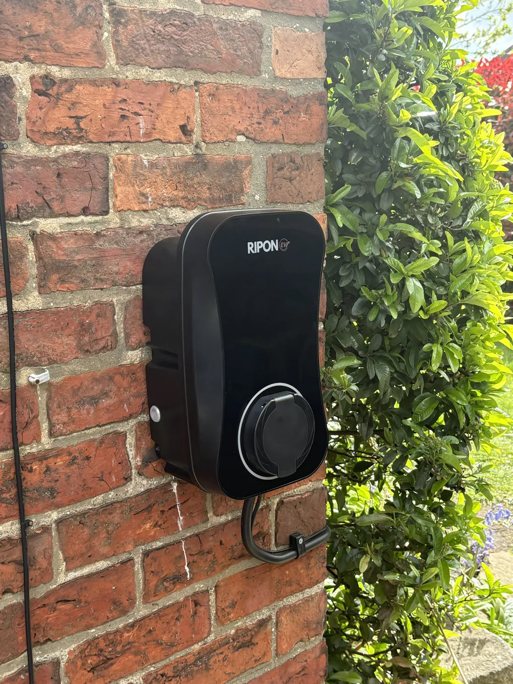 RiponEV untethered charger on an old red brick wall beside a hedge