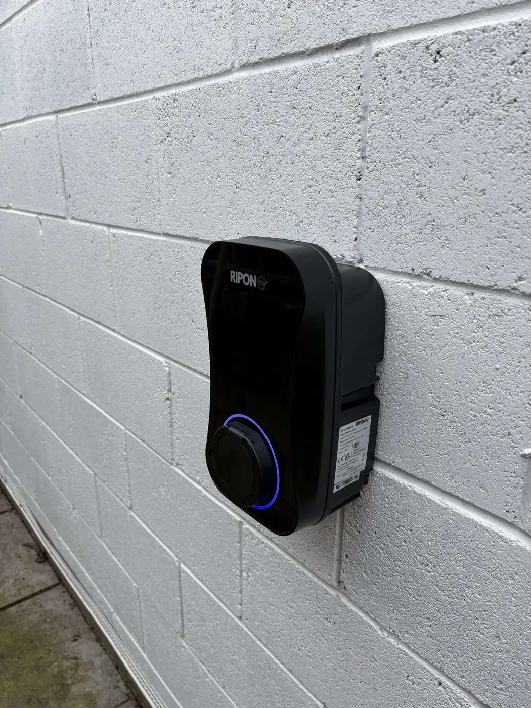 Side view of a RiponEV charger on a painted block wall, blue ring lit