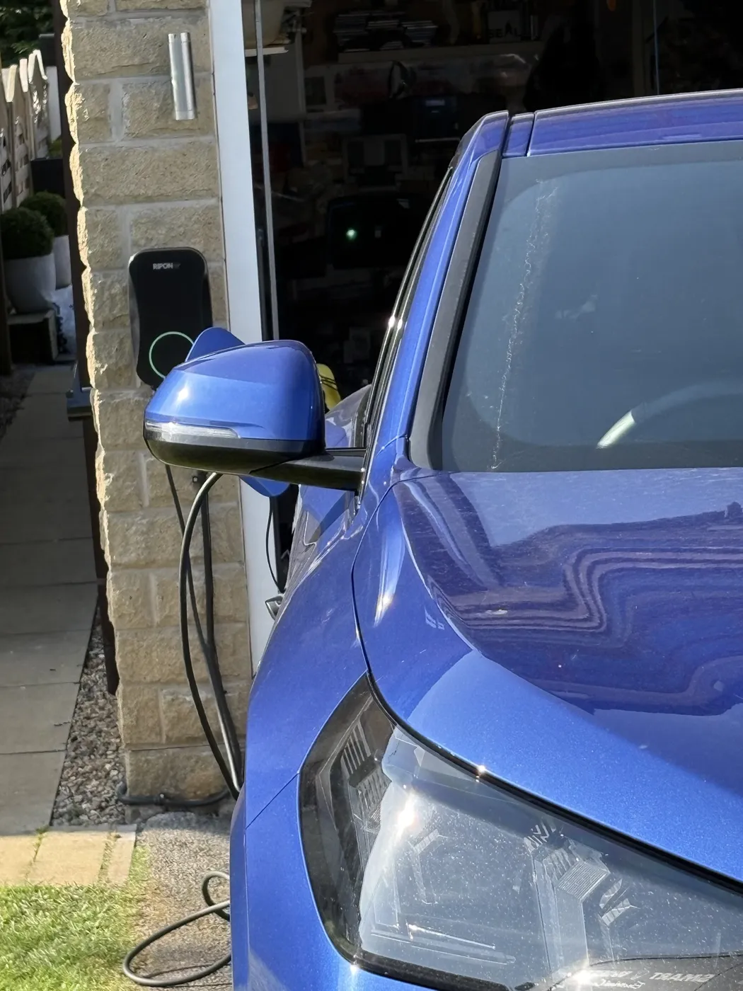 Blue electric car plugged into a RiponEV charger on a stone garage wall