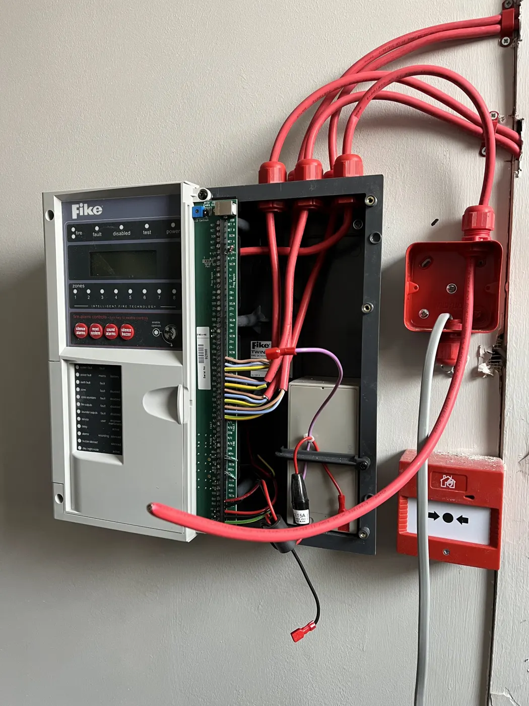 Fike fire alarm panel open during installation, with red fire-resistant cables and a call point