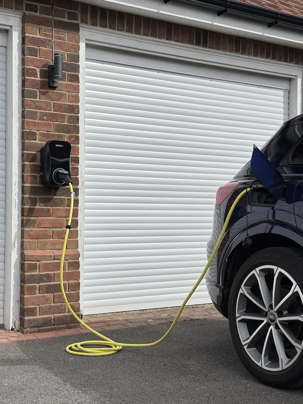 Untethered RiponEV charger on a brick garage pier with the car’s own cable plugged in