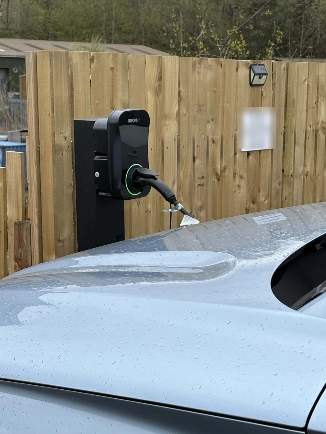 RiponEV charger on a freestanding black post beside a parking bay, car plugged in