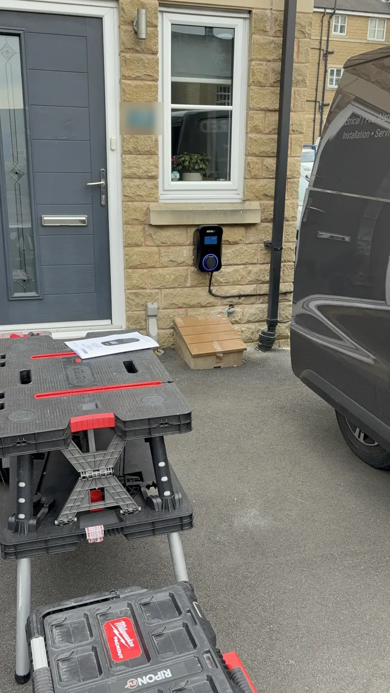 RiponEV display charger on the stone front of a new-build home in Huddersfield, with the SmartWired van on the drive