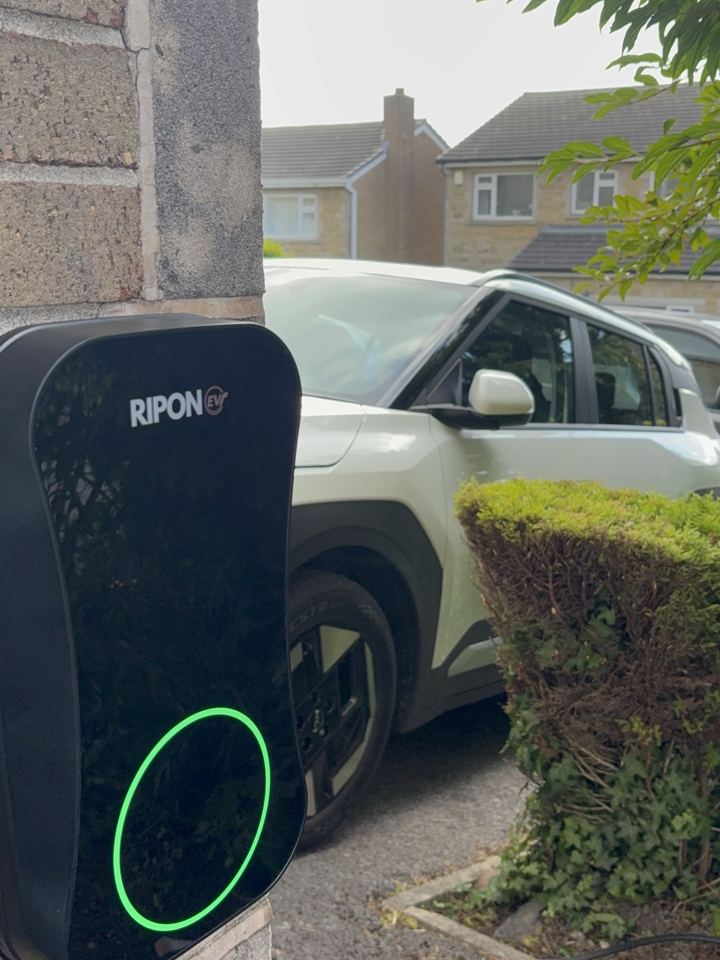 EV charger with green charging light beside a driveway