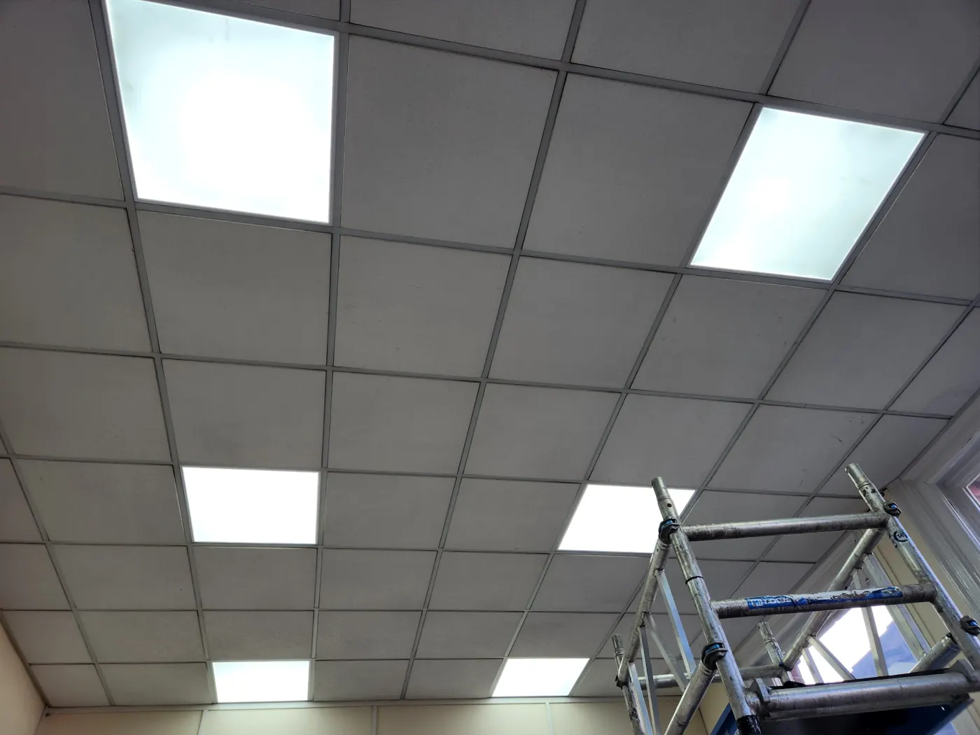 Office ceiling grid fitted with new LED panels, tower scaffold in place