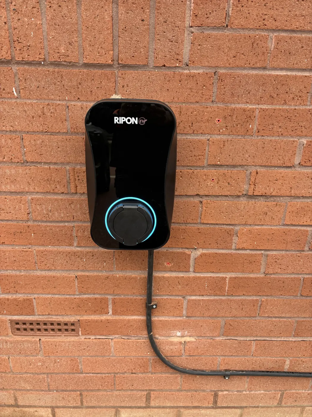 Untethered RiponEV charger on red brick with cable clipped neatly