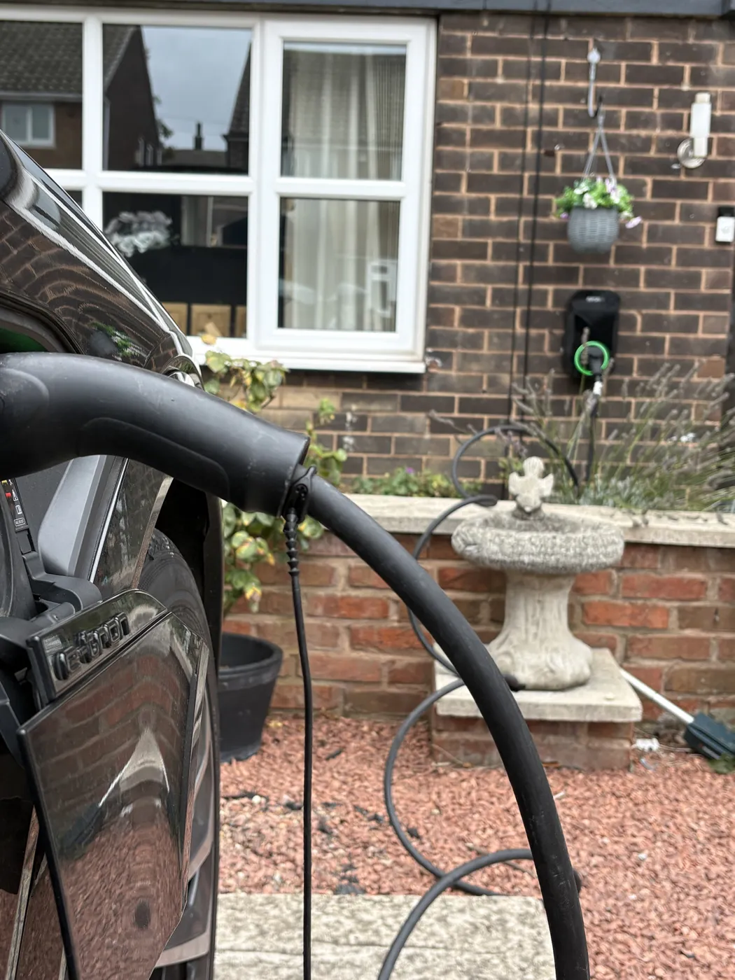 Audi e-tron plugged in and charging from a RiponEV charger on a dark brick house