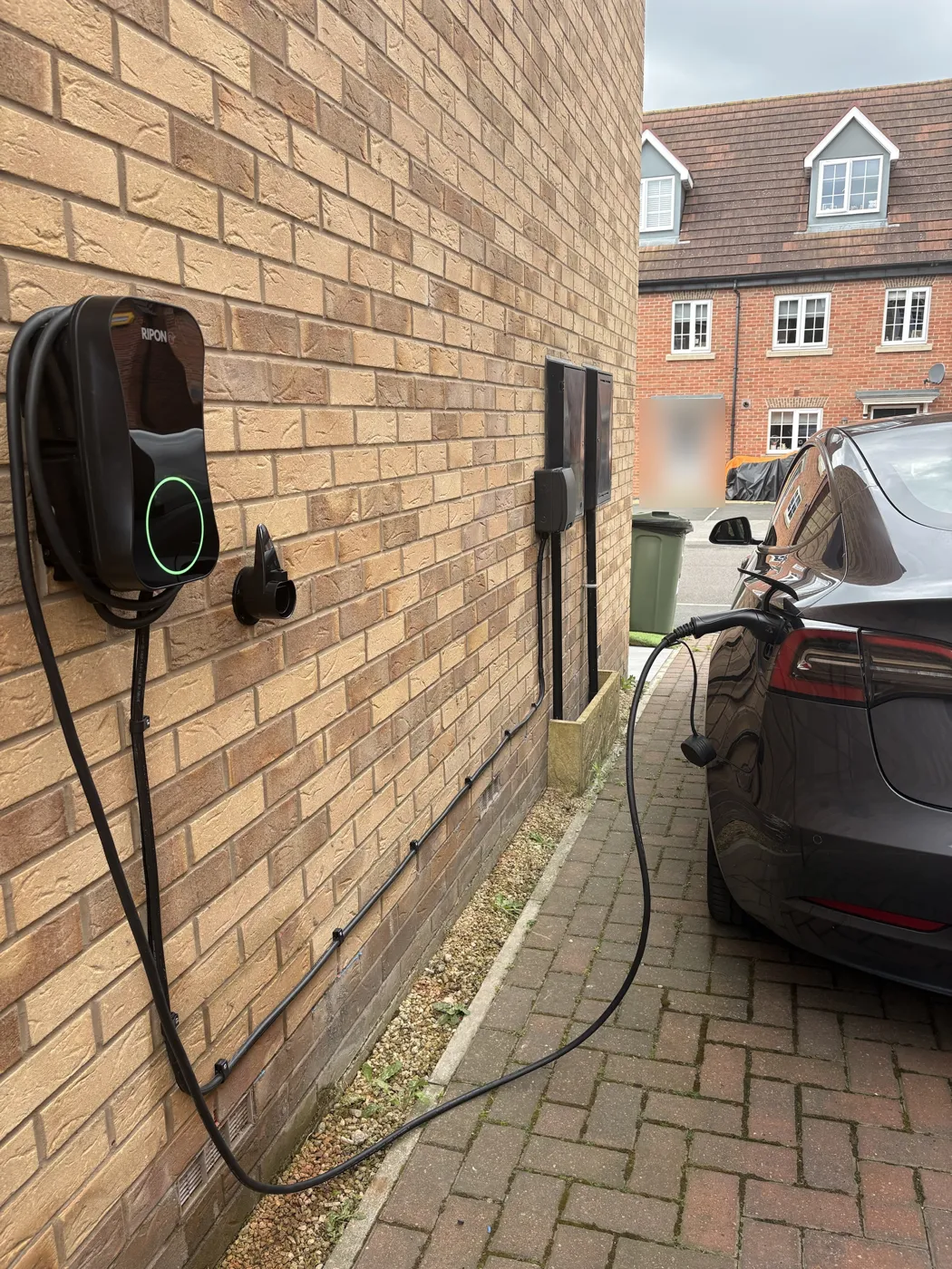 Tesla charging from a tethered RiponEV charger on the side of a new-build house in Wakefield